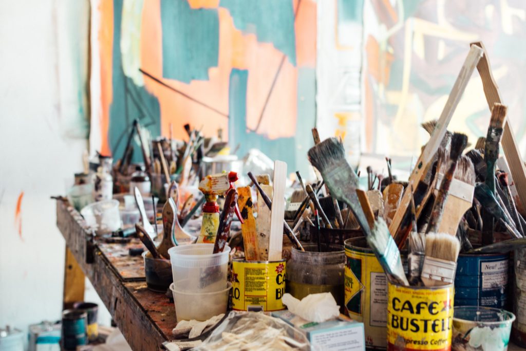 messy artist table with brushes in coffee cans